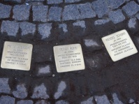 Drei Stolpersteine liegen auf einem gepflasterten Boden
