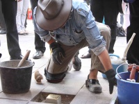 Ein Mann mit Hut kniet auf dem Boden und verlegt einen Stolperstein