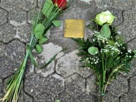Stoplerstein auf gepflastertem Boden umgeben von einer roten und weißen Rosen
